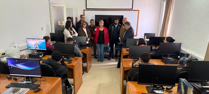 Salón de clases con autoridades y jóvenes en escritorios con su computadora